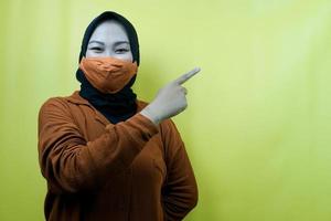 muslimische Frau mit Maske, mit der Hand, die auf den leeren Raum zeigt, der etwas präsentiert, isoliert foto