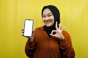 schöne junge asiatische muslimische frau, die ein smartphone mit weißem oder leerem bildschirm hält, app fördert, etwas fördert, isoliert, werbekonzept