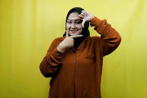 schöne und fröhliche junge asiatische muslimische Frau mit Kameraporträt-Geste, isoliert foto