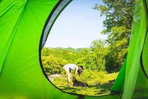 Blick vom Zelt auf die junge Frau, die mit ihrem Hund spielt, isoliert in grüner Natur foto