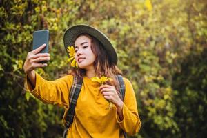 Ein Mädchen mit einem Rucksack macht mit dem Telefon ein Selfie von der gelben Bua-Tong-Blume. mexikanische Sonnenblume foto