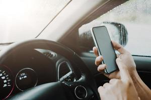 Hand der Frau am Lenkrad Auto fahren, während sie das Smartphone benutzt. foto