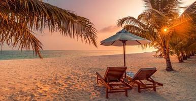 wunderschöne tropische Sonnenuntergangslandschaft, zwei Sonnenliegen, Liegestühle, Sonnenschirm unter Palmen. weißer Sand, Meerblick mit Horizont, bunter Dämmerungshimmel, Ruhe und Entspannung. inspirierendes Strandresorthotel foto