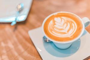 Latte Art in Cappuccino-Kaffeetasse am Café-Tisch. Nahaufnahme der Rosetta-Blumenzeichnung in Schaum. Idyllische Morgenstimmung, Vibes, Chillen, Relaxen foto