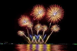 erstaunliches schönes buntes Feuerwerk in der Feiernacht, das am Meeresstrand mit mehrfarbiger Reflexion auf dem Wasser gezeigt wird foto