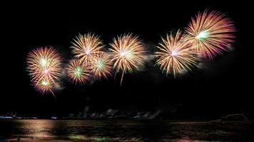 erstaunliches schönes buntes Feuerwerk in der Feiernacht, das am Meeresstrand mit mehrfarbiger Reflexion auf dem Wasser gezeigt wird foto