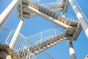 Treppe Metall Struktur draussen - - ein kleiner Winkel Aussicht von ein Metall Treppe führen nach oben, mit ein hell Blau Himmel im das Hintergrund. das Treppe sind gemacht von Metall und haben ein Geländer. foto