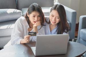 Zwei junge Frauen benutzen einen Laptop, um online über das Internet einzukaufen, während sie zu Hause sicher bleiben foto