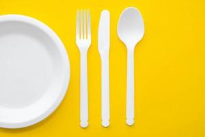 weiße Plastikgabel, Messer, Löffel und Teller auf gelbem Hintergrund. Koch Utensilien. Ansicht von oben. minimalistischer Stil. kopieren, leerer Platz für Text
