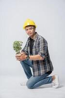 Ein Mann trägt orangefarbene Handschuhe und sitzt, um einen Blumentopf im Haus zu halten. foto