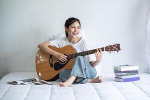 das Mädchen saß und spielte Gitarre auf dem Bett. foto
