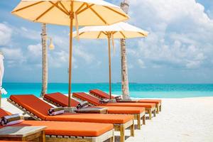 Strand ruhige Szene mit Sonnenliegen unter Kokospalmen in der Nähe des Swimmingpools und der Ozeanlagune. weißer Sand, sonniges Wetter, Sommerurlaub Resort Hotelkonzept