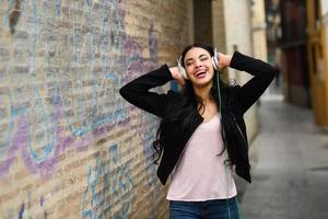 Frau im städtischen Hintergrund, die mit Kopfhörern Musik hört foto