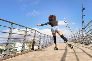 Rückansicht der schwarzen Frau auf Rollschuhen, die auf der städtischen Brücke reitet. foto