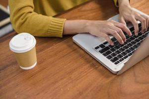Nahaufnahme einer jungen Frau, die mit dem Laptop auf einem Schreibtisch im Café arbeitet. junge frau, die am wochenende mit ihrem laptop an einem warmen sonnenlichttag arbeitet. Laptop, der im Coffeeshop-Konzept arbeitet.