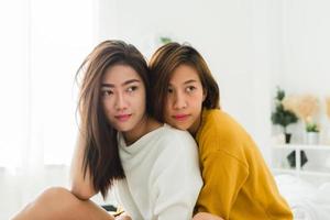 schöne junge asiatische frauen lgbt lesbisches glückliches paar sitzen auf dem bett, umarmen und lächeln zusammen im schlafzimmer zu hause. lgbt lesbisches paar zusammen drinnen konzept. schöne Zeit zu Hause verbringen. foto