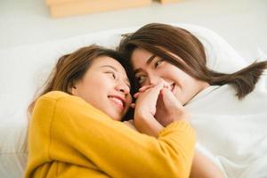schöne junge asiatische frauen lgbt lesbisches glückliches paar umarmen und lächeln, während sie zu hause zusammen im bett unter der decke liegen. lustige Frauen nach dem Aufwachen. lgbt lesbisches paar zusammen drinnen konzept. foto