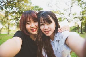 Zwei schöne glückliche junge asiatische Freundinnen, die zusammen Spaß im Park haben und ein Selfie machen. glückliche Hipster junge asiatische Mädchen, die Kamera lächeln und betrachten. Lifestyle- und Freundschaftskonzepte. foto