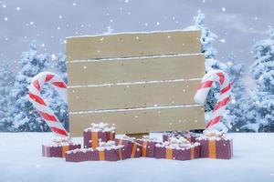 Holzschild über einer verschneiten Landschaft mit Weihnachtsgeschenken foto