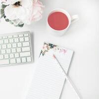 Weißer Arbeitsplatz mit hellrosa Notizbuch und weißer Blume mit Kaffee auf weißem Tisch. foto