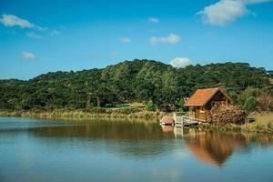 cambara do sul, brasilien - 18. juli 2019. kleine rustikale hütte spiegelt sich auf dem see mit kristallklarem wasser und hügeln, die von einem wald in der nähe von cambara do sul bedeckt sind. foto