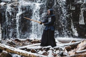 Mann, der Kendo mit Bambusschwert auf Wasserfallhintergrund übt foto