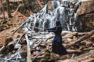 Mann, der Kendo mit Bambusschwert auf Wasserfallhintergrund übt foto