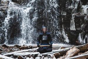 Mann, der Kendo mit Bambusschwert auf Wasserfallhintergrund übt foto