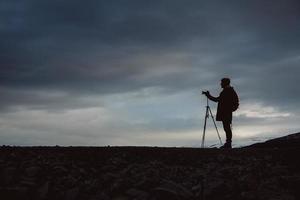 Silhouette eines männlichen Reisenden mit Kamera auf Stativ auf dramatischem Himmelshintergrund