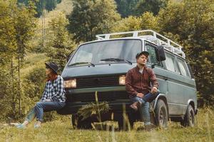 Mann und Frau sitzen in der Nähe von Van auf Bergen und Waldhintergrund foto