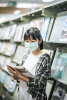 eine Frau, die eine Maske trägt und in der Bibliothek nach Büchern sucht.