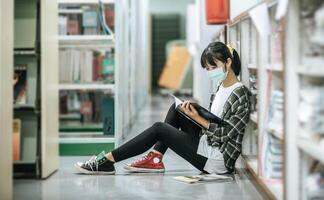 Eine maskierte Frau sitzt in der Bibliothek und liest ein Buch. foto