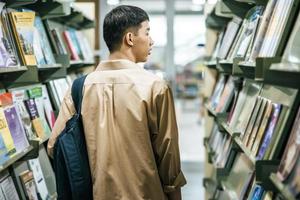 Männer, die einen Rucksack tragen und in der Bibliothek nach Büchern suchen.