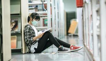 Eine maskierte Frau sitzt in der Bibliothek und liest ein Buch. foto