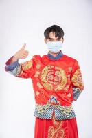 Mann trägt Cheongsam-Anzug und Maske zeigt den besten Weg zum Einkaufen zum Schutz von Krankheiten foto