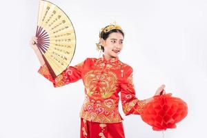Frau trägt Cheongsam-Anzug halten den chinesischen Handfächer und die rote Lampe, um auf einem großen Ereignis im chinesischen Neujahr zu zeigen