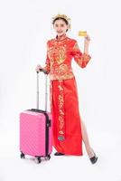 Frau trägt Cheongsam-Anzug mit Krone bereiten Sie rosa Reisetasche und Kreditkarte für die Reise im chinesischen Neujahr vor foto