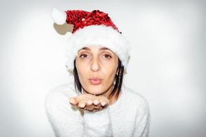 Frau mit Weihnachtsmütze sendet im weißen Hintergrund isolierten Kuss. Geschenke und Liebeskonzept an Weihnachtsfeiertagen. foto