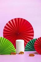 weißes zylindrisches Podest mit rotem, grünem Papierfächerhintergrund für Branding und Produktpräsentation. Chinesische Manets Hochformat. Nahansicht foto
