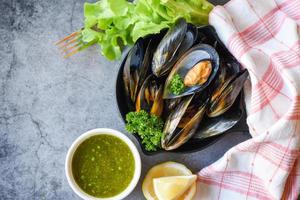 gekochte Muscheln mit Kräuterzitrone und dunklem Tellerhintergrund - frische Meeresfrüchte auf Schüssel und würziger Saucensalat im Restaurant Muschelschalenessen