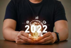 Geschäftsmann, der eine helle Glühbirne mit den Zielen des neuen Jahres 2022 für Finanz- und Geschäftswachstum hält Geschäftsideen und -ziele des neuen Jahres 2022 foto