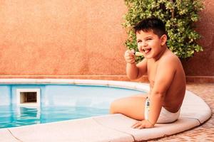 glücklicher kleiner Junge im Pool beim Eisessen foto