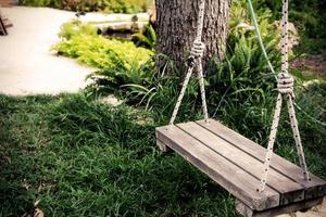 alte hölzerne Vintage-Schaukel, die an einem großen Baum im Garten mit grünem Grashintergrund hängt foto