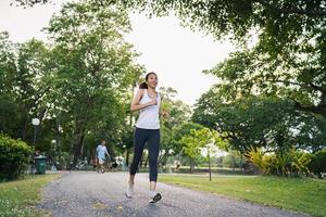 Gesunde schöne junge asiatische Läuferin in Sportkleidung, die morgens auf dem Bürgersteig in der Nähe des Sees im Park läuft und joggt. Lifestyle-Fitness und aktive Frauen trainieren im urbanen Stadtkonzept. foto