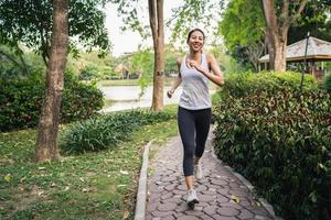 Gesunde schöne junge asiatische Läuferin in Sportkleidung, die morgens auf dem Bürgersteig in der Nähe des Sees im Park läuft und joggt. Lifestyle-Fitness und aktive Frauen trainieren im urbanen Stadtkonzept. foto