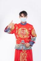 Mann trägt Cheongsam-Anzug und Maske zeigt den besten Weg zum Einkaufen zum Schutz von Krankheiten foto