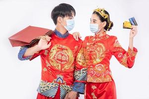 Männer und Frauen tragen Qipao und Gesichtsmasken, tragen Papiertüten, gehen mit Kreditkarten einkaufen. foto