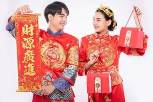 Männer und Frauen, die Cheongsam im Stehen tragen, Grußschilder halten und rote Taschen tragen foto