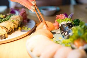 eine Person, die Sushi in einem Restaurant isst. sichtbare Essstäbchen, die nach Sushi greifen. foto