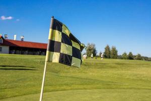 eine karierte Flagge auf einem Golfplatz, die ein Loch gegen ein Goldgebäude anzeigt foto
